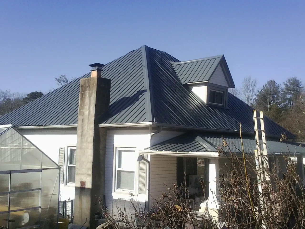 Dark blue standing seam metal roof on a white farmhouse with dormer — Slate & Tile Roof Repair by Roofing Brothers in Kittredge
