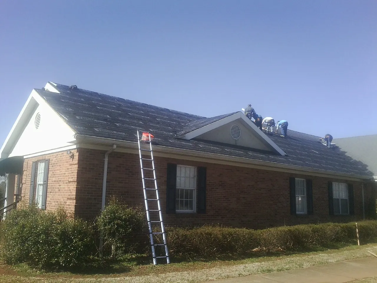 Crew tearing shingles off a brick ranch roof with a ladder set — Emergency Roof Repair work by our crew in Kittredge