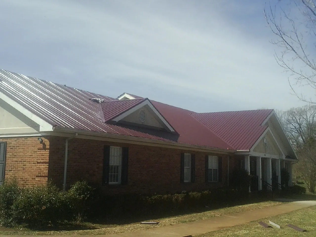 Red metal roof with gabled entries on a long brick building, from a Hail Damage Roof Repair job in Kittredge