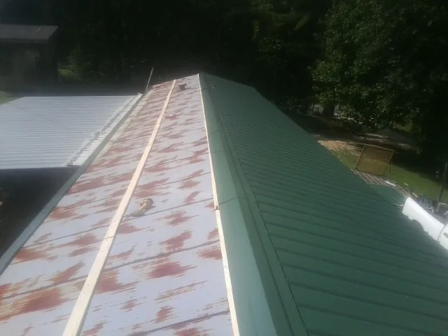 Old rusted panels beside newly installed green metal roofing — Wind Damage Roof Repair by Roofing Brothers in Kittredge