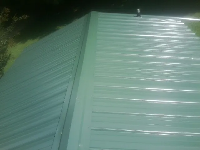 New green metal panels meeting at the ridge of a roof — Flat Roof Repair work by our crew in Kittredge