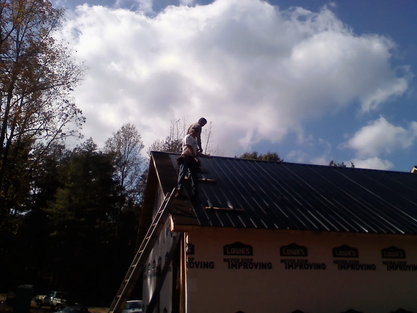 Roofer fastening dark metal panels high against a cloudy sky, from a Roof Inspection job in Kittredge