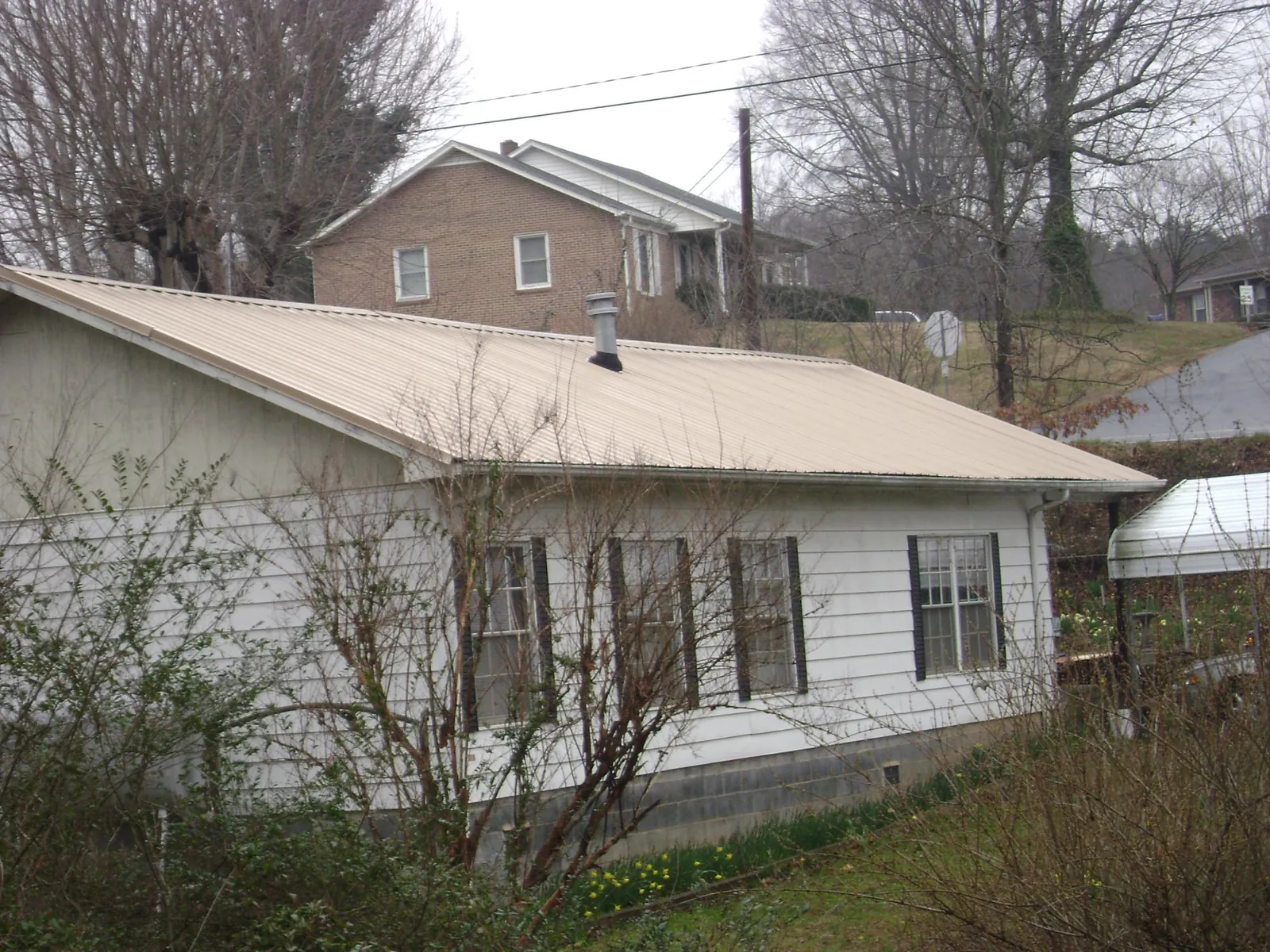 Tan metal roof on a white sided house set into a hillside — Commercial Roofing by Roofing Brothers in Kittredge
