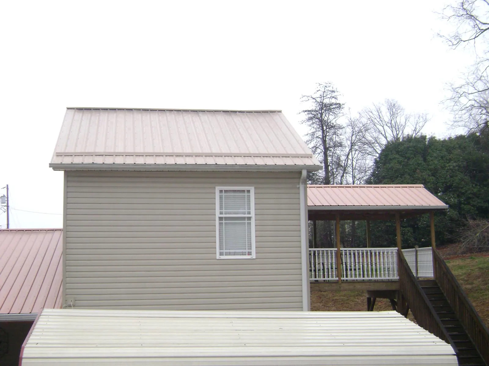 Tan metal roofs on a two story addition and attached porch, from a Roof Replacement job in Kittredge